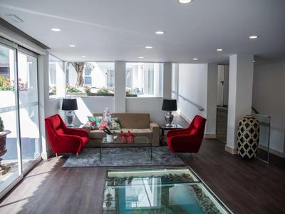 Heller Hotellobbybereich mit Glasboden, roten Sesseln und Sofa vor großen Fenstern.