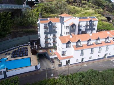 Großes Hotelgebäude mit roten Dächern und Außenpool in grüner Landschaft