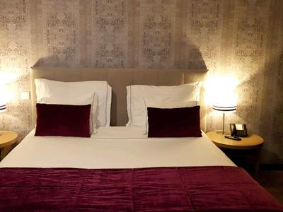 Gemütliches Doppelbett mit weißen und dunkelroten Kissen und warmem Licht am Nachttisch.