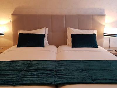 Zwei Einzelbetten mit weißen Bettlaken und grünen Akzentkissen in modernem Hotelzimmer.