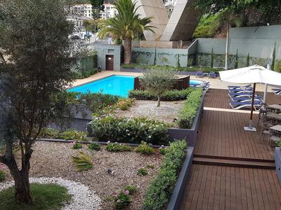 Blick auf einen Bereich mit Pool, Garten und Sonnenschirmen auf einer Holzterrasse.