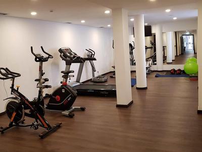 Fitnessraum mit mehreren stationären Fahrrädern und Laufbändern vor weißen Wänden und Holzfußboden