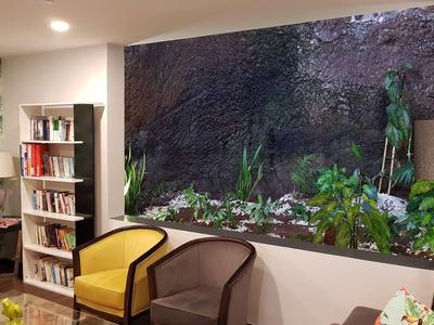 Ein gemütliches Wohnzimmer mit zwei Sesseln, Bücherregal und einem großen Fenster mit Blick auf einen Garten.