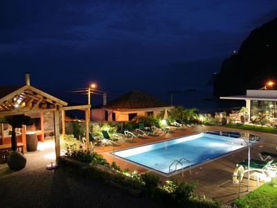 Illuminated hotel pool area at night with lounge chairs and a pavilion.