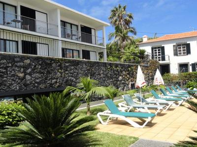 Hotel garden with lounge chairs, umbrellas, and green plants under sunny weather