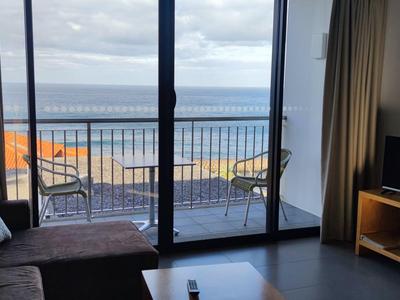 View from a hotel room with sofa, TV, and balcony overlooking the sea.