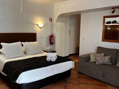Hotel room with large bed, gray sofa, and warm-toned tiled floor.