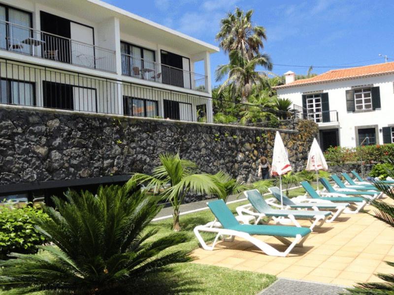Hotel garden with lounge chairs, umbrellas, and green plants under sunny weather