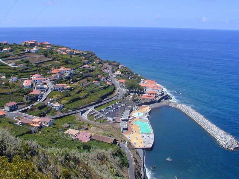 Coastal town with harbor, swimming pool, and houses on a hill by the sea
