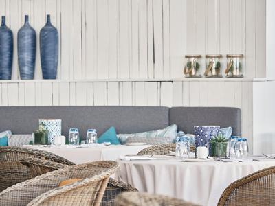 Accogliente zona pranzo con tavoli rotondi, sedie in vimini e decorazioni blu sulla parete.