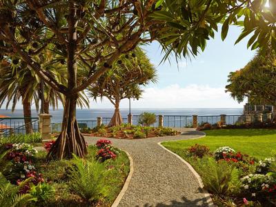 Sentiero lastricato che attraversa un giardino tropicale con vista sul mare sullo sfondo.