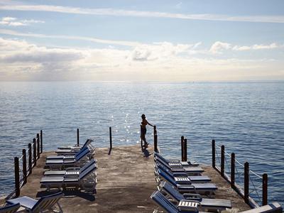 Persona in piedi alla fine di un molo con sedie a sdraio, che guarda il mare al tramonto.