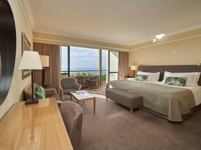 Spaziosa camera d'albergo con letto grande, area salotto e balcone con vista sul mare.