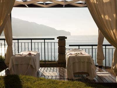 Due lettini da massaggio su una terrazza con vista sul mare e sulle montagne al tramonto.