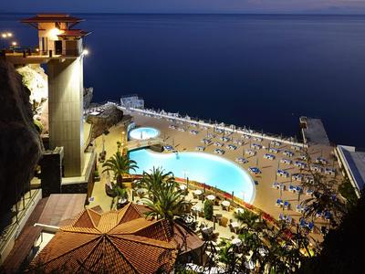 Vista serale di una piscina illuminata e una spiaggia con molte sedie a sdraio vicino al mare.