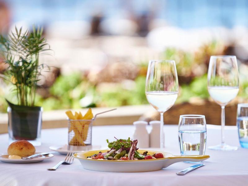 Tavolo elegantemente apparecchiato con insalata, panino, posate e bicchiere in un ristorante con vista esterna.