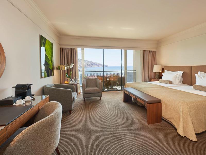 Camera d'hotel moderna con letto matrimoniale, area salotto e balcone con vista mare.