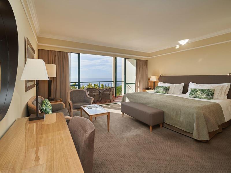 Spaziosa camera d'albergo con letto grande, area salotto e balcone con vista sul mare.