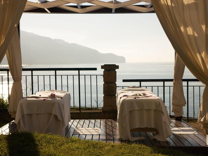 Due lettini da massaggio su una terrazza con vista sul mare e sulle montagne al tramonto.