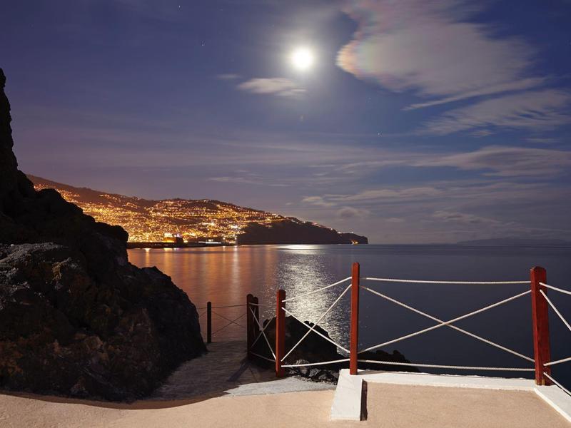 Vista costiera notturna con città illuminata sotto chiaro di luna e mare calmo