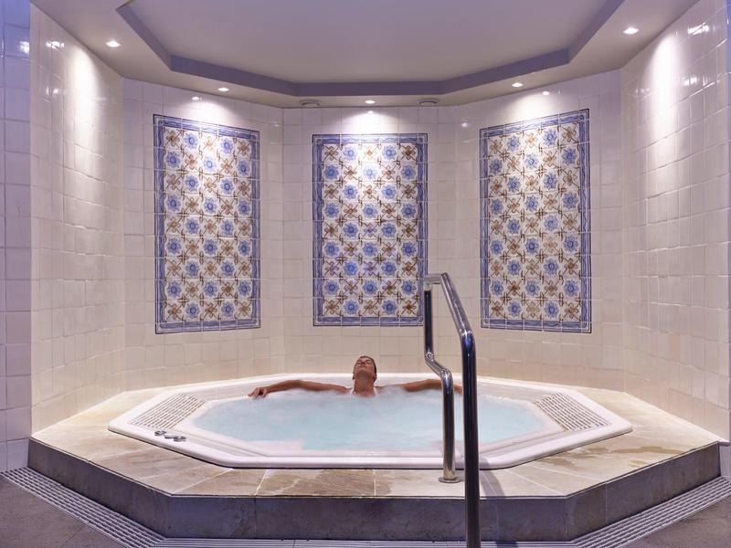 Persona che si rilassa in una vasca idromassaggio riscaldata con piastrelle decorative.