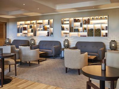 Moderní hotelová lobby s šedými křesly a dekorativním nástěnným osvětlením.