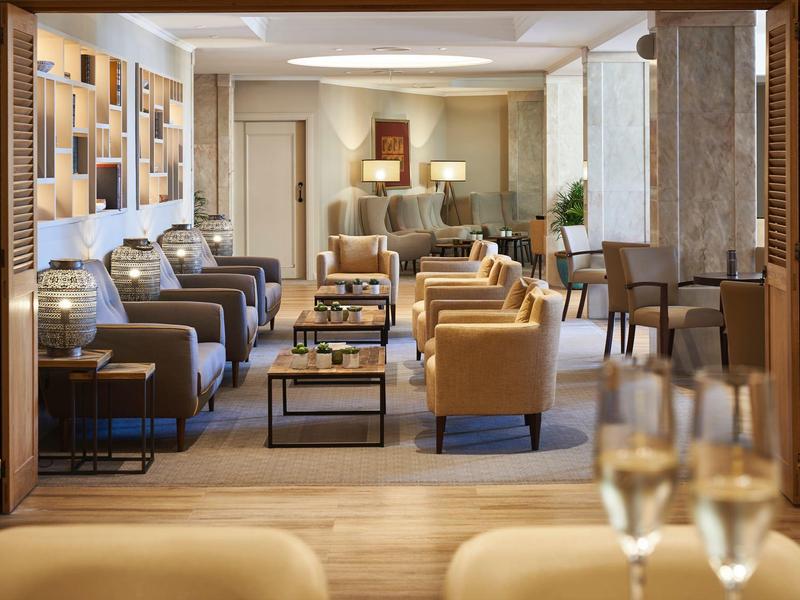 Elegantní hotelový salon s pohodlnými křesly a moderními stolky ve teplém osvětlení.