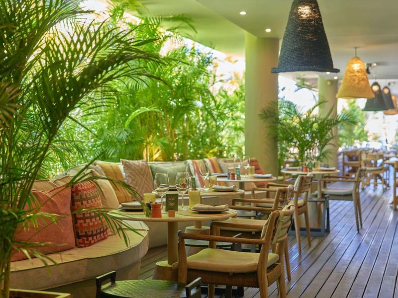 Příjemný venkovní prostor restaurace s dřevěnou podlahou, rostlinami a pohodlným sezením.