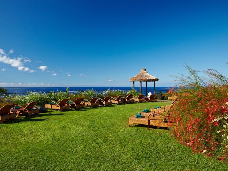 Zelený hotelový trávník s lehátky a výhledem na modré moře pod jasnou oblohou.