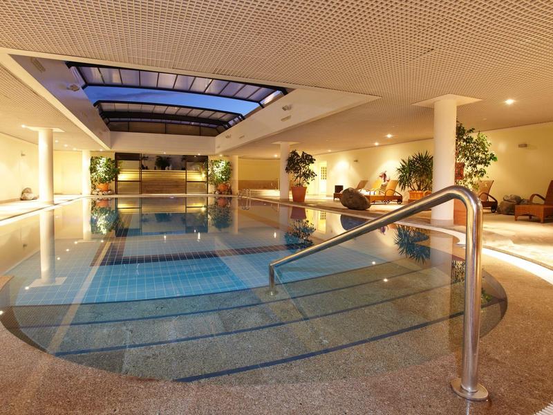 Vnitřní bazén se schody, skleněnou střechou a odpočinkovou plochou v hotelu.