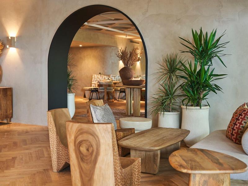 Pohodlná lounge s dřevěnými židlemi, pohovkami a květináči v teplém osvětlení.