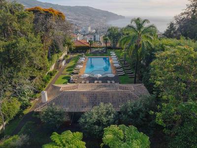 Großer Garten mit Pool, umgeben von Bäumen, Palmen und Bergen im Hintergrund.