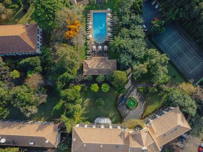 Luftaufnahme eines Gartens mit Pool, Tennisplatz, mehreren Häusern und viel grünem Pflanzenbewuchs.