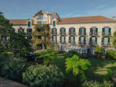 Großes dreistöckiges Gebäude mit roten Ziegeldächern, vielen Fenstern und grünem Garten davor.