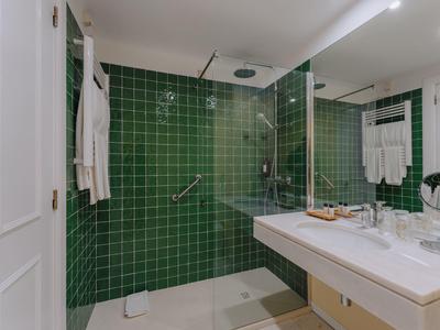 Modernes Badezimmer mit grünen Fliesen, Glasdusche, großem Spiegel und weißem Waschtisch.