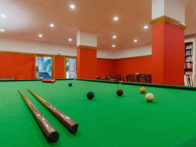 Wnętrze z zielonym stołem bilardowym, czerwonymi ścianami i oświetleniem sufitowym.