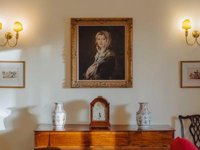 Elegantes Wohnzimmer mit antiker Kommode, zwei Lampen, Vase und klassischem Gemälde an der Wand.