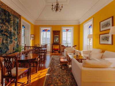 Helles Wohnzimmer mit gelben Wänden, antiken Holzmöbeln und großem Teppich auf Holzboden.