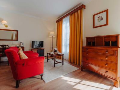 Wohnzimmer mit rotem Sessel, Holzmöbeln, gelben Vorhängen und hellem Holzboden.