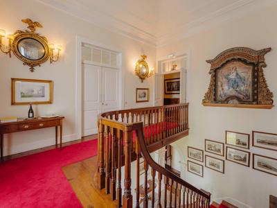 Heller Flur mit rotem Teppich, Holztreppe, antiken Spiegeln und gerahmten Bildern an den Wänden.