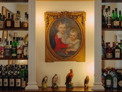 Bar mit Holzregalen voller Flaschen, kleines Gemälde von Mutter und Kind, Figuren auf Tresen.