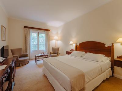 Gemütliches Hotelzimmer mit großem Bett, zwei Sesseln, Schreibtisch und Beleuchtung.