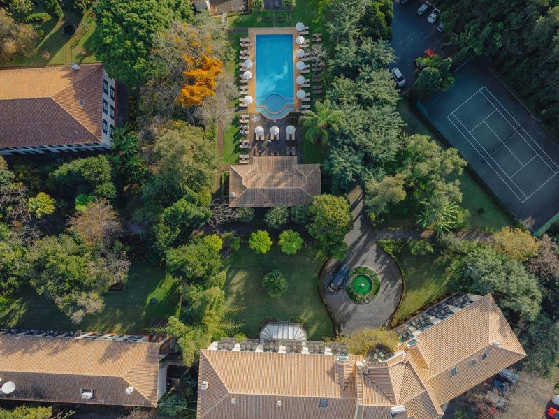 Luftaufnahme eines Gartens mit Pool, Tennisplatz, mehreren Häusern und viel grünem Pflanzenbewuchs.