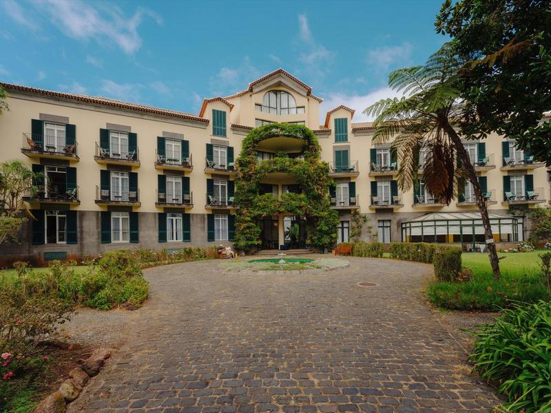 Großes dreistöckiges Gebäude mit vielen Fenstern, umgeben von Bäumen und gepflastertem Weg.