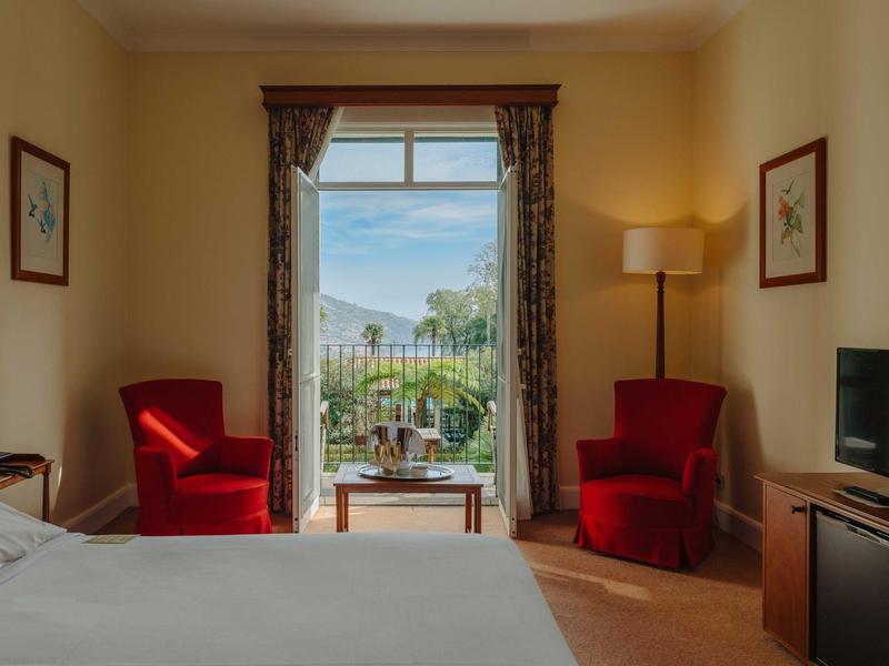 Gemütliches Schlafzimmer mit zwei roten Sesseln, großem Bett und Balkon mit Bergblick.