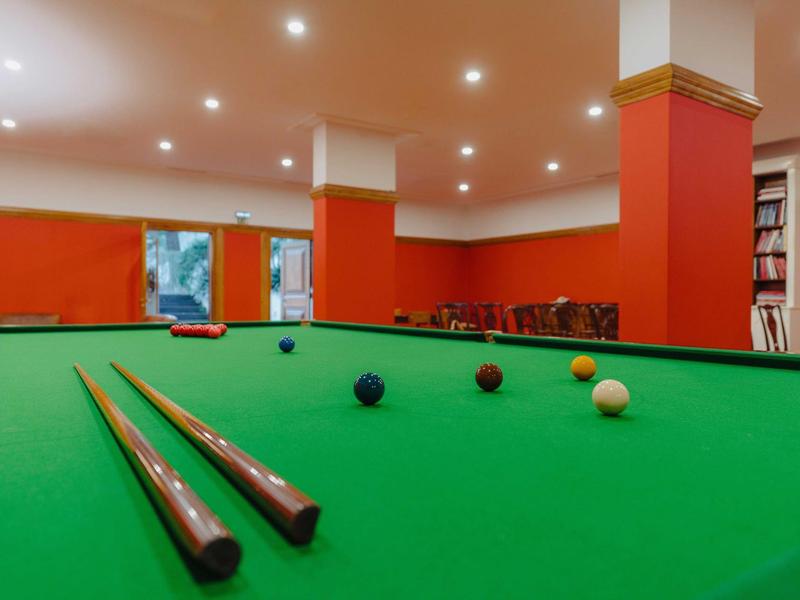 Billardtisch mit grünem Tuch, zwei Queues und mehreren farbigen Kugeln in einem roten Raum.