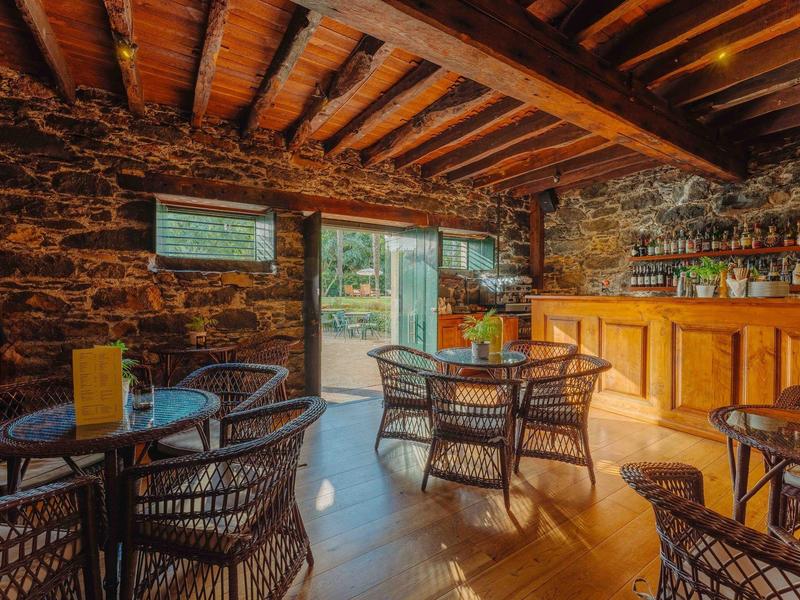 Gemütliche Bar mit Steinwänden, Holzbalkendecke, Tresen und Rattanstühlen an runden Tischen.