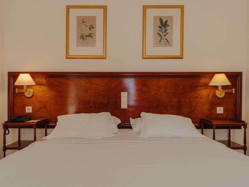Hotelzimmer mit Doppelbett, Holzkopfteil, Nachttischen und zwei Bilderrahmen an der Wand.