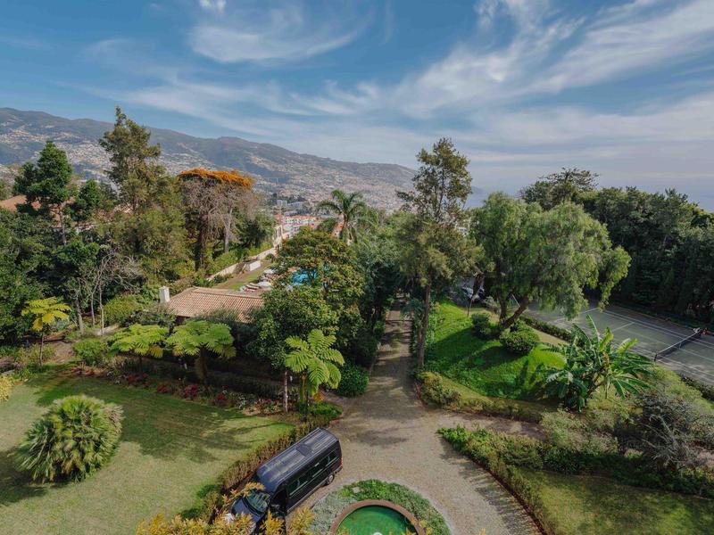Grüner Park mit Bäumen, Wasserbecken und Berglandschaft unter blauem Himmel.