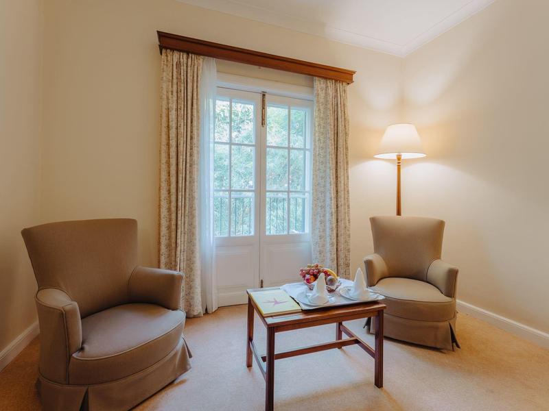 Gemütlicher Raum mit zwei braunen Sesseln, Holztisch und großem Fenster mit hellen Vorhängen.